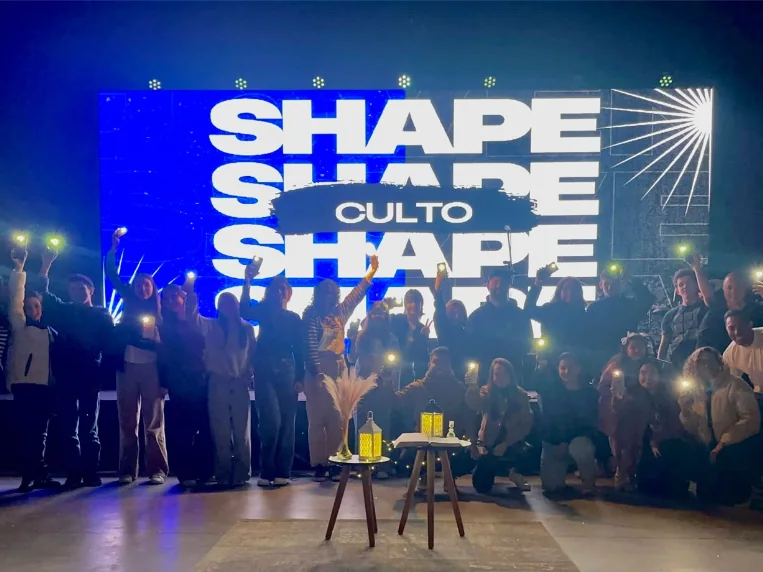 Participantes reunidos diante do telão do culto Shape