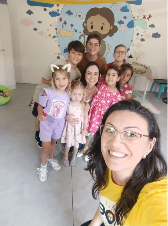 Crianças e adultas reunidas em uma sala infantil com ilustração de Jesus